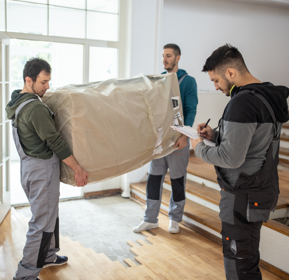 Workers moving a large wrapped package indoors.