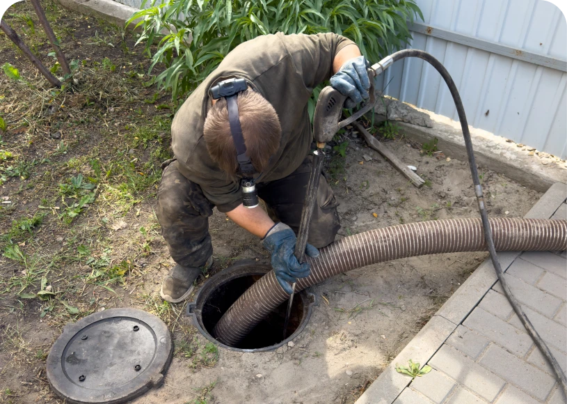 Worker cleaning a septic tank with hose.