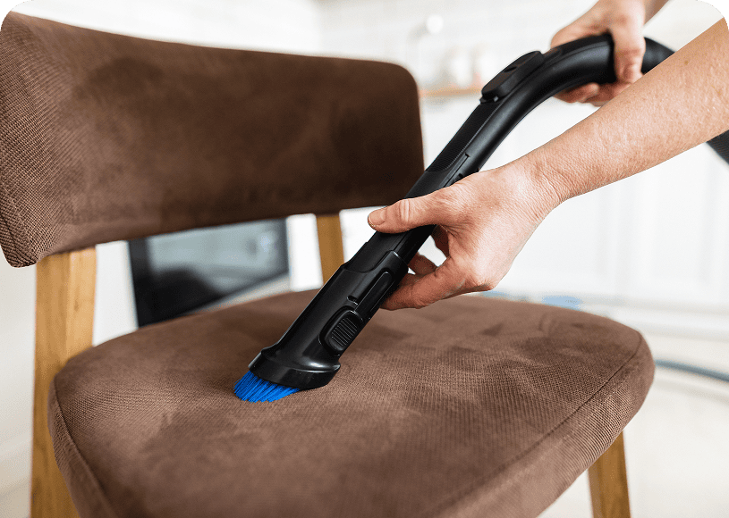 Vacuuming a brown chair with brush attachment.