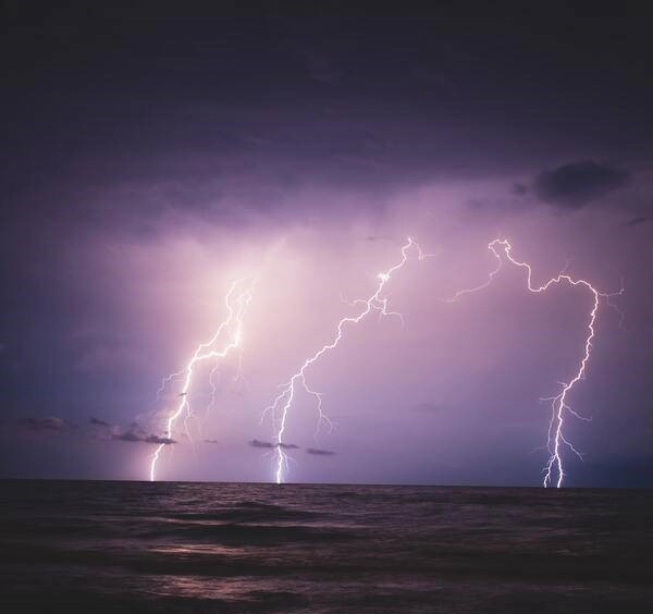 Lightning strikes over the ocean at night.