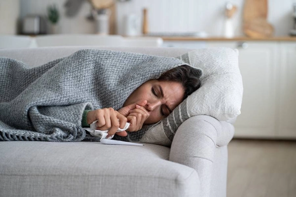 Person ill on couch under gray blanket.