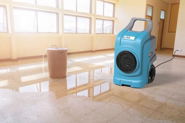 Dehumidifier drying wet floor in empty room.