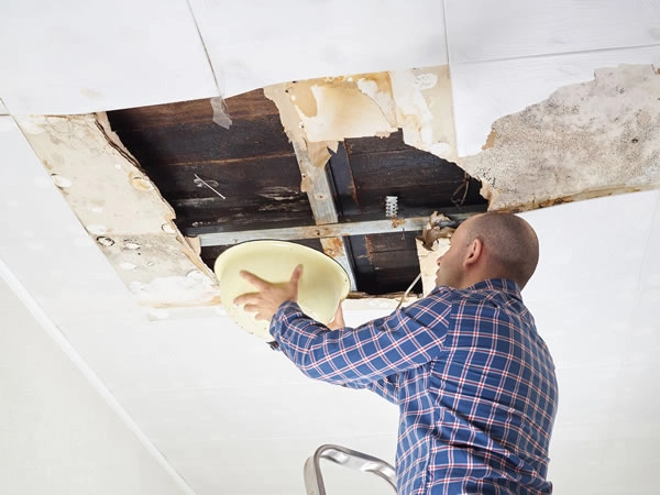 Man repairing damaged ceiling with ladder.