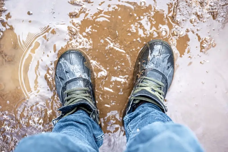 Boots standing in muddy water puddle.
