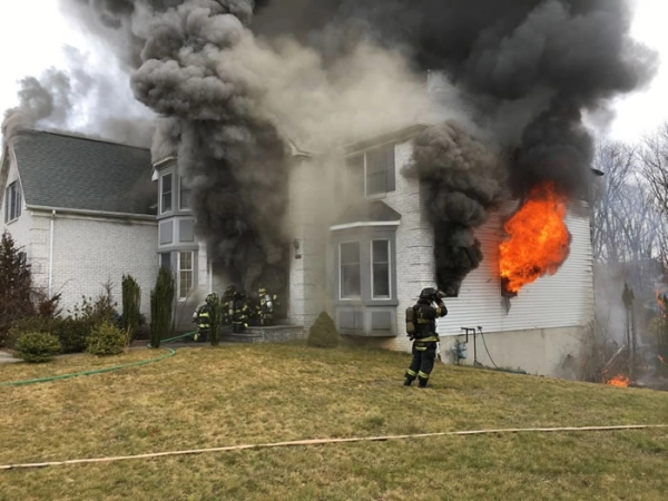 Firefighters tackling large house fire with smoke.
