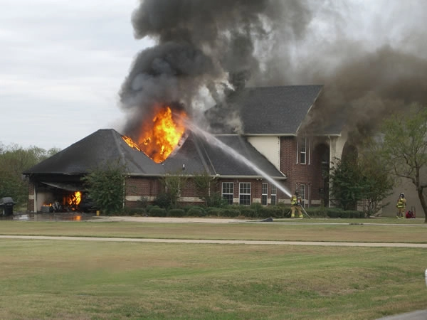 House on fire with firefighters extinguishing blaze.