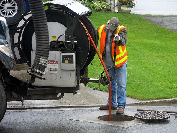 Worker cleaning sewer with vacuum truck.