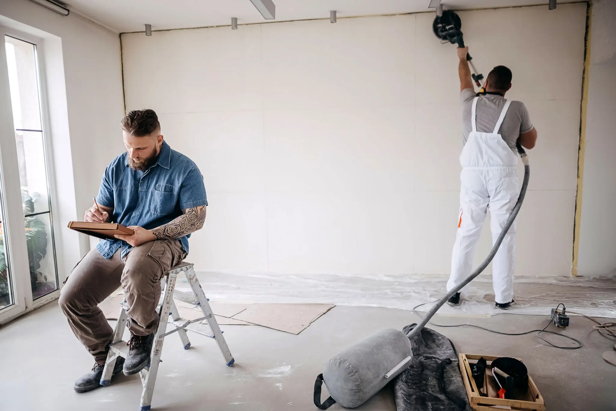 Man sitting on a ladder in a room, holding a clipboard and pen