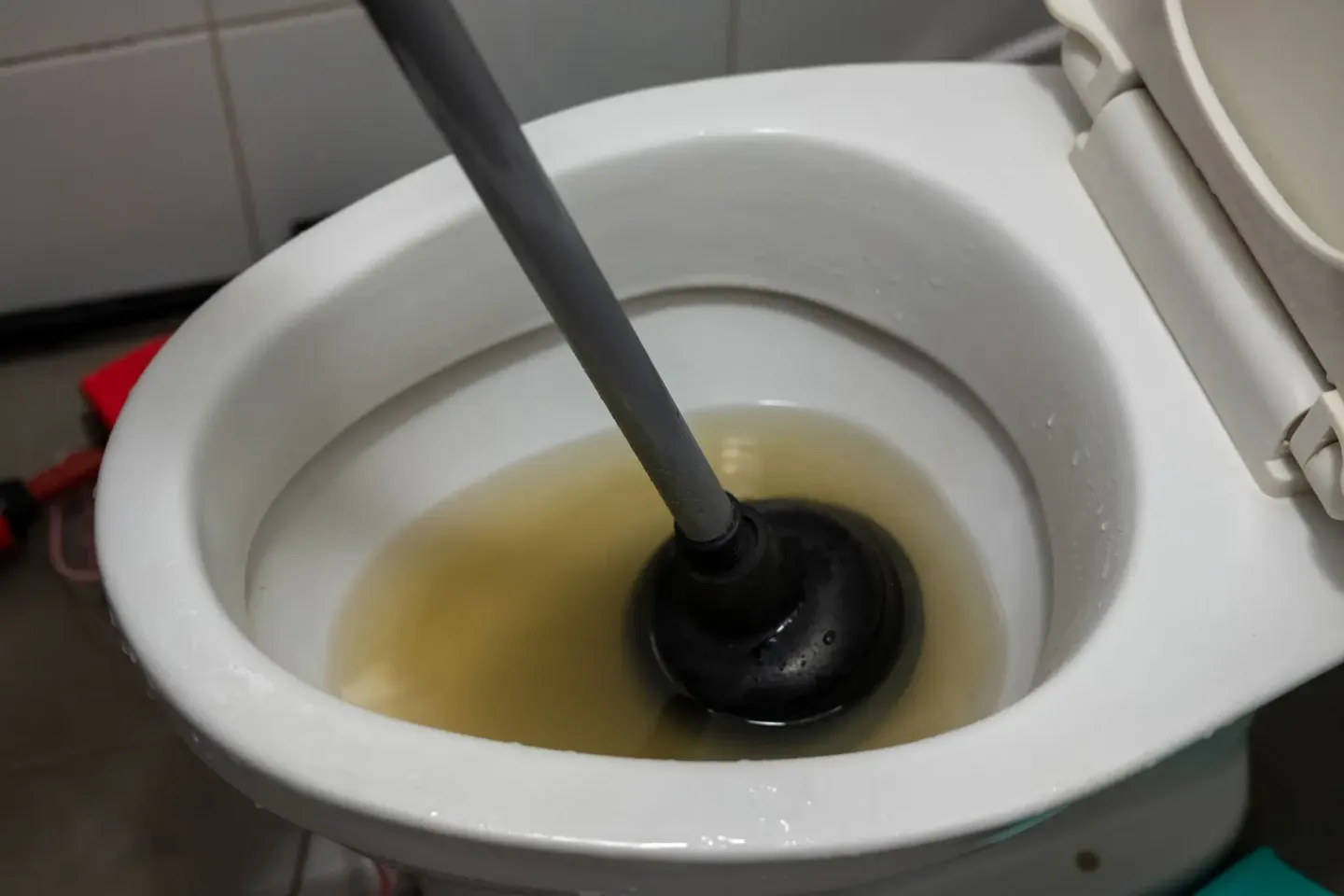 Toilet with a plunger in the middle of it, surrounded by a wall in the background
