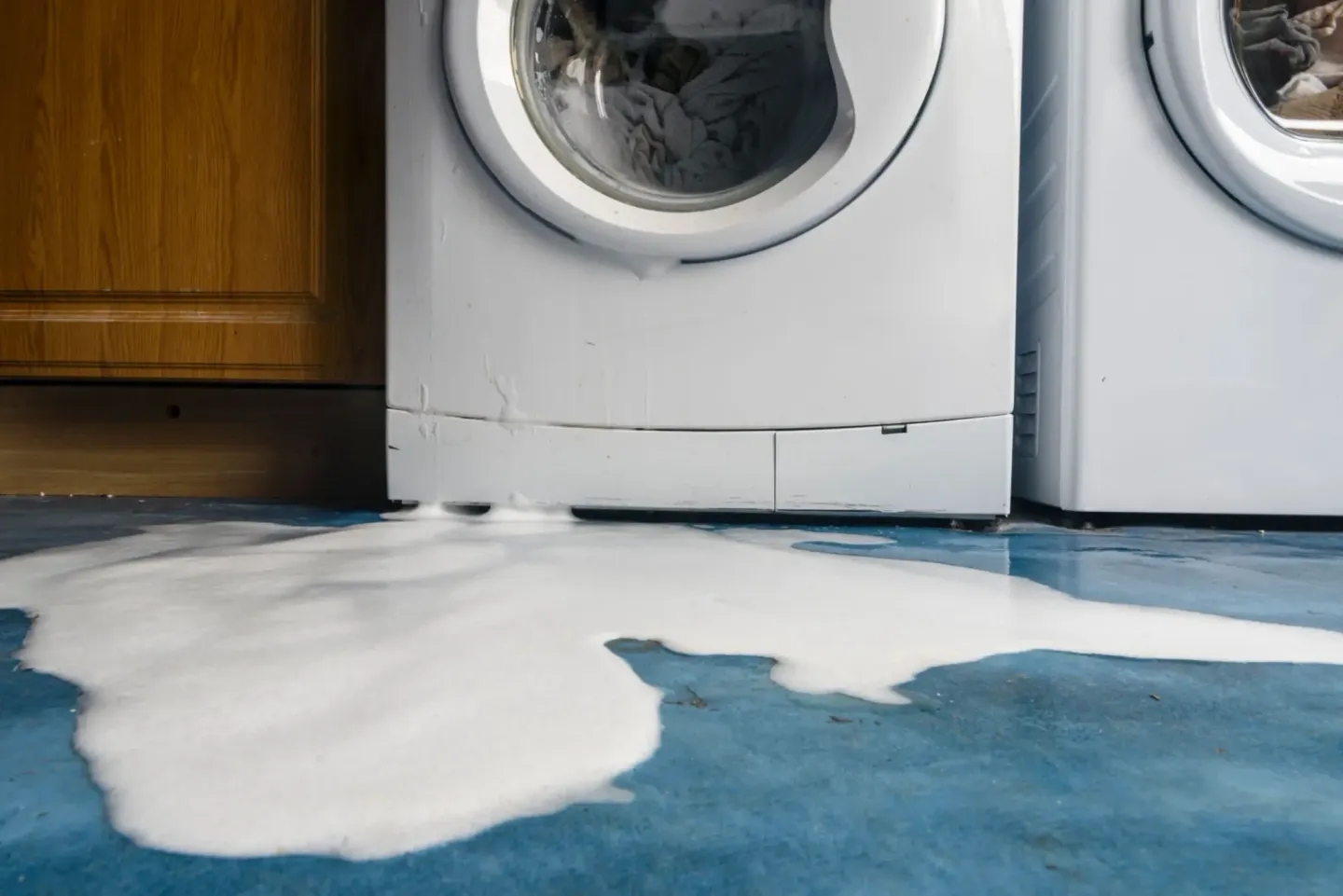 Washing machine sitting next to a blue floor with a puddle of water on it