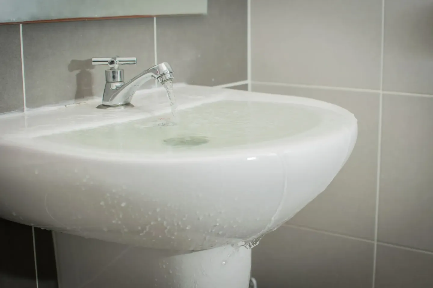White sink sitting under a mirror in a bathroom, with water flowing from the tap into the wash basin