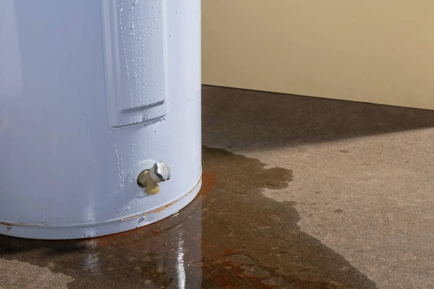 White water heater sitting on top of a cement floor, with a wall in the background